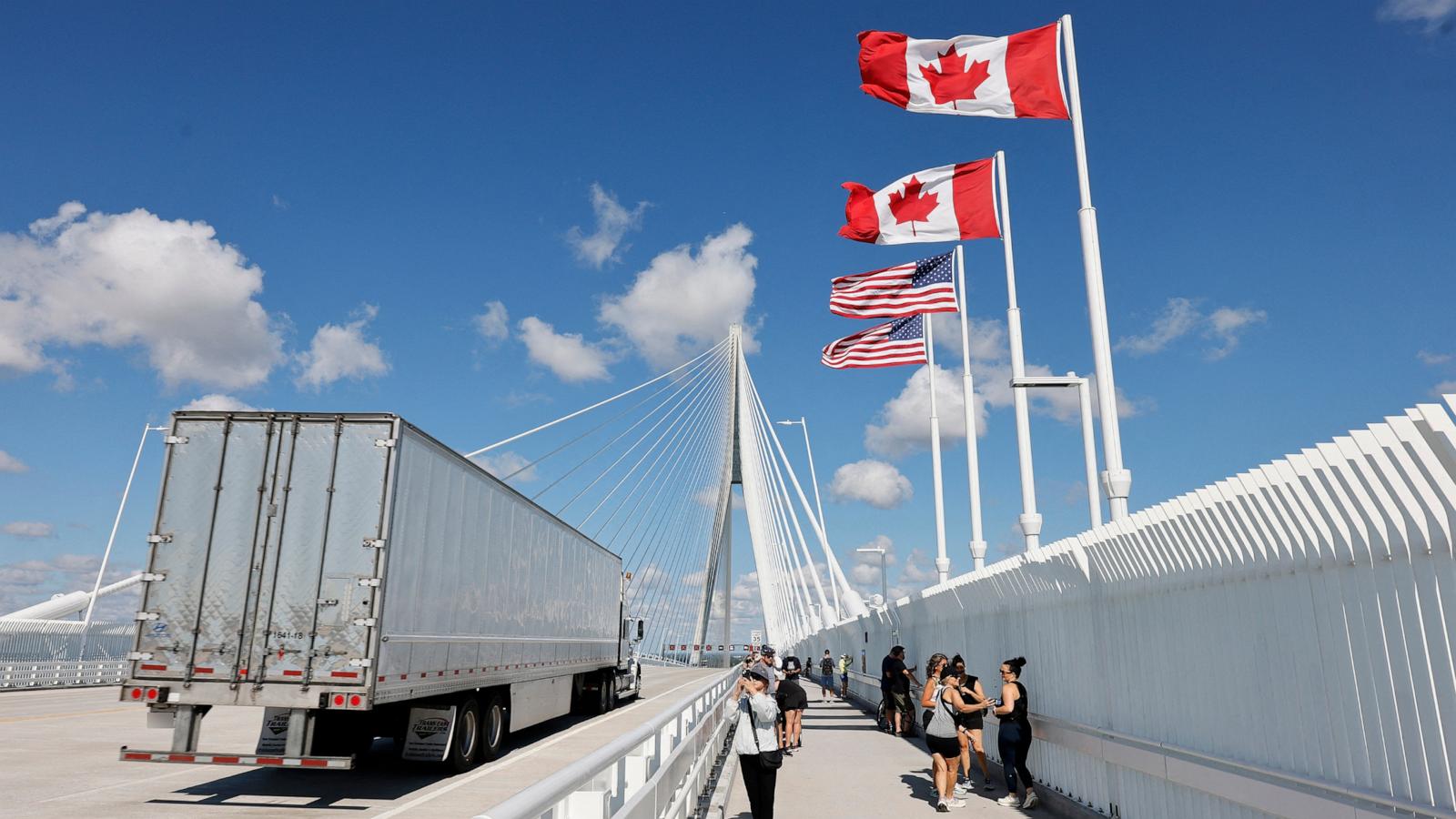Canadian and American flags fly beside a truck crossing a cable-stayed border bridge.
