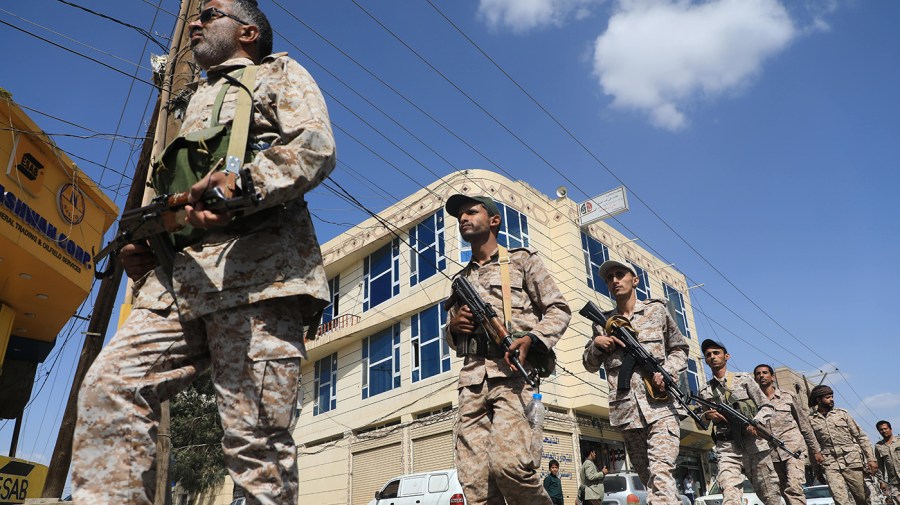 Armed fighters in desert camouflage stand guard along a street.