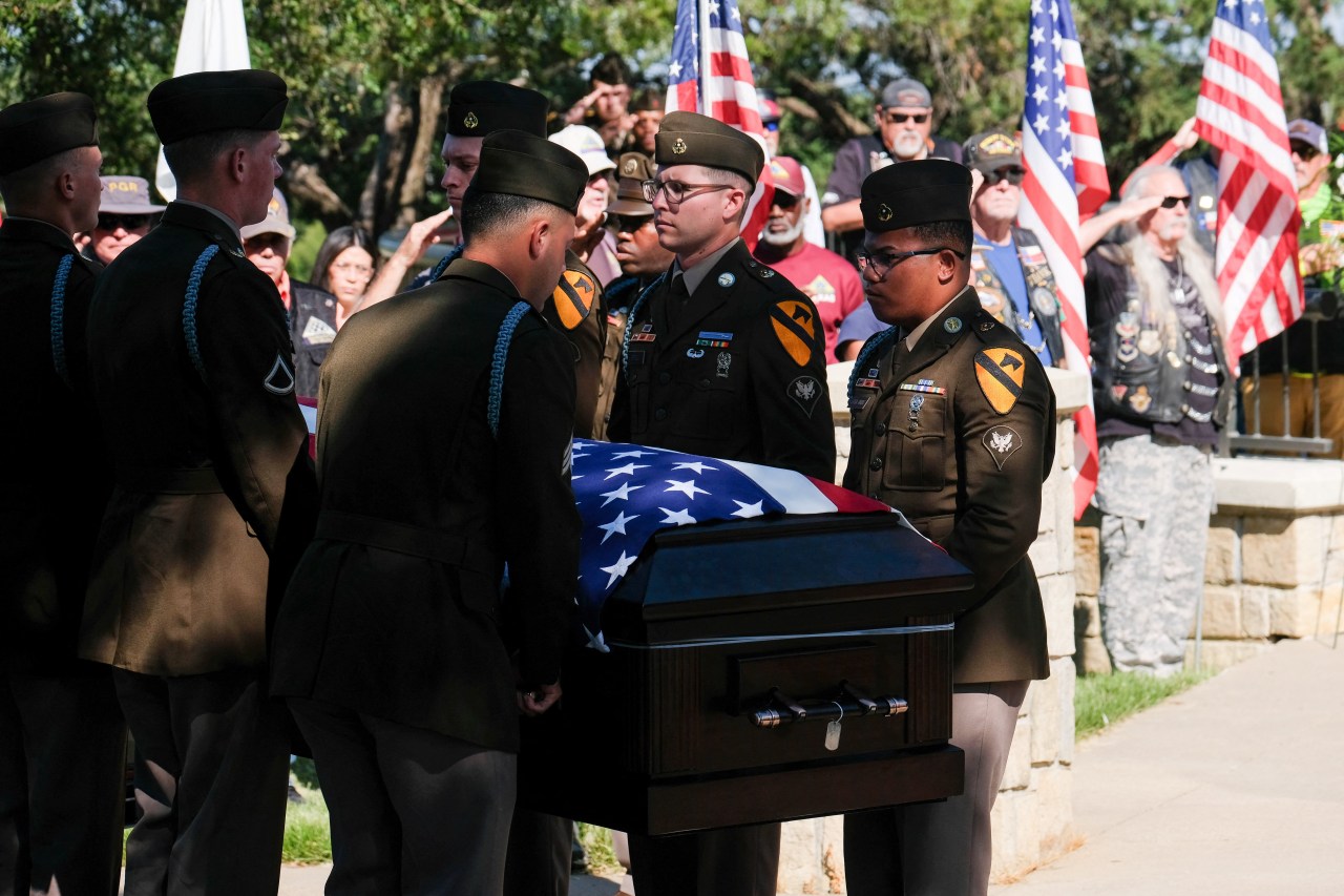 An honor guard carries a flag-draped casket at a dignified transfer.