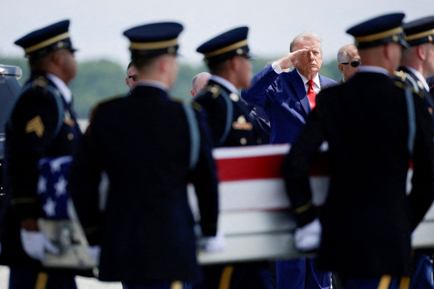 Uniformed service members salute as a flag-draped case is carried between them during a dignified transfer.