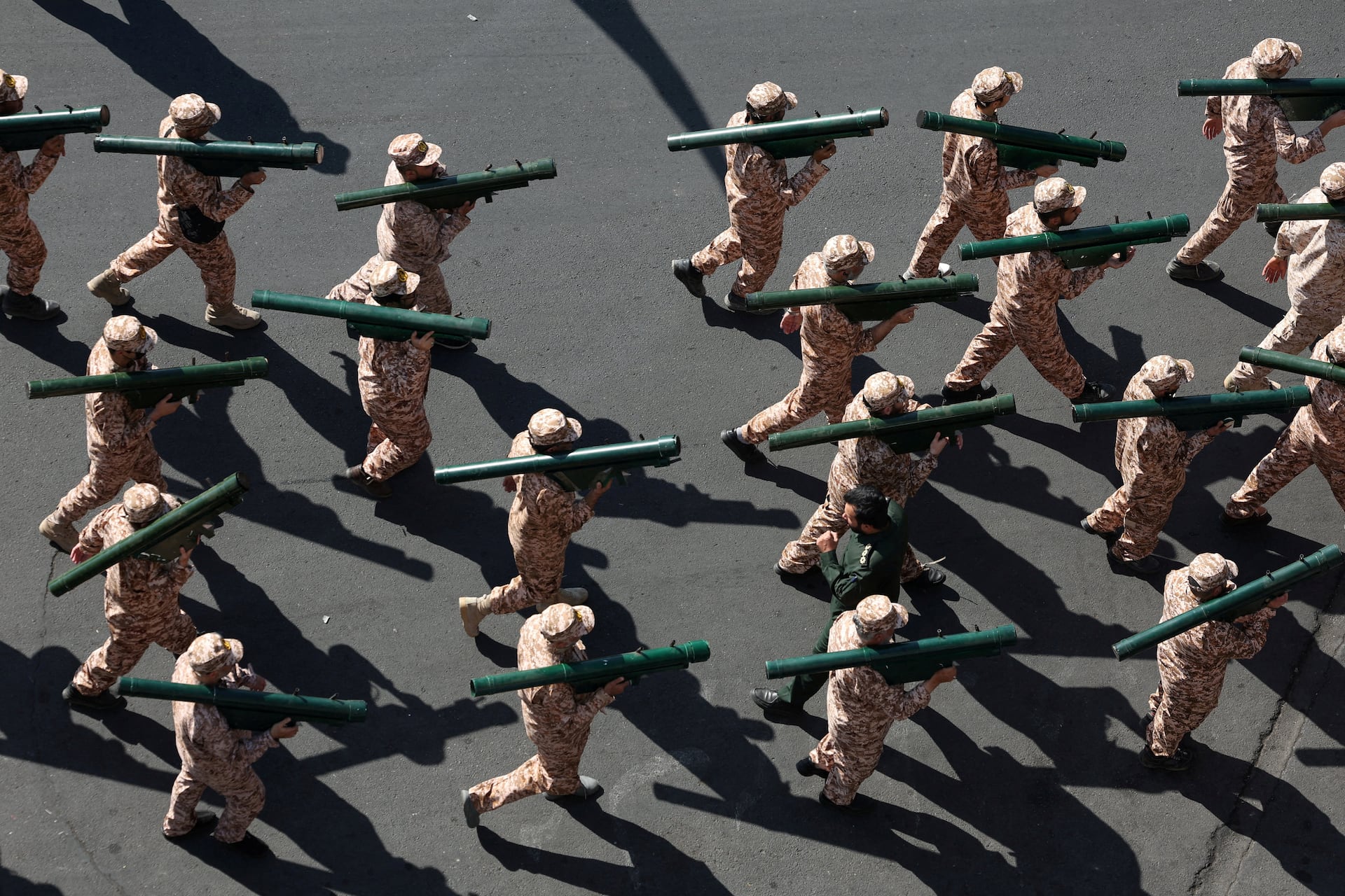 Uniformed fighters march in formation carrying shoulder-fired rocket launchers, seen from above.