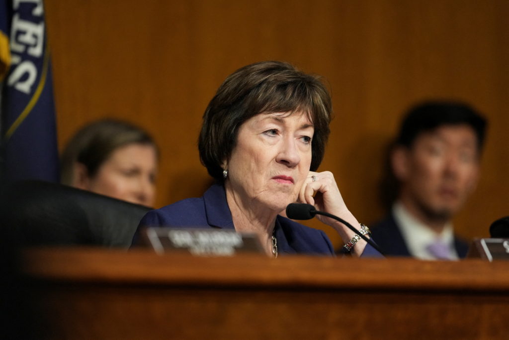 Sen. Susan Collins (R-Maine) rests her hand against her face while seated behind a microphone at a hearing.