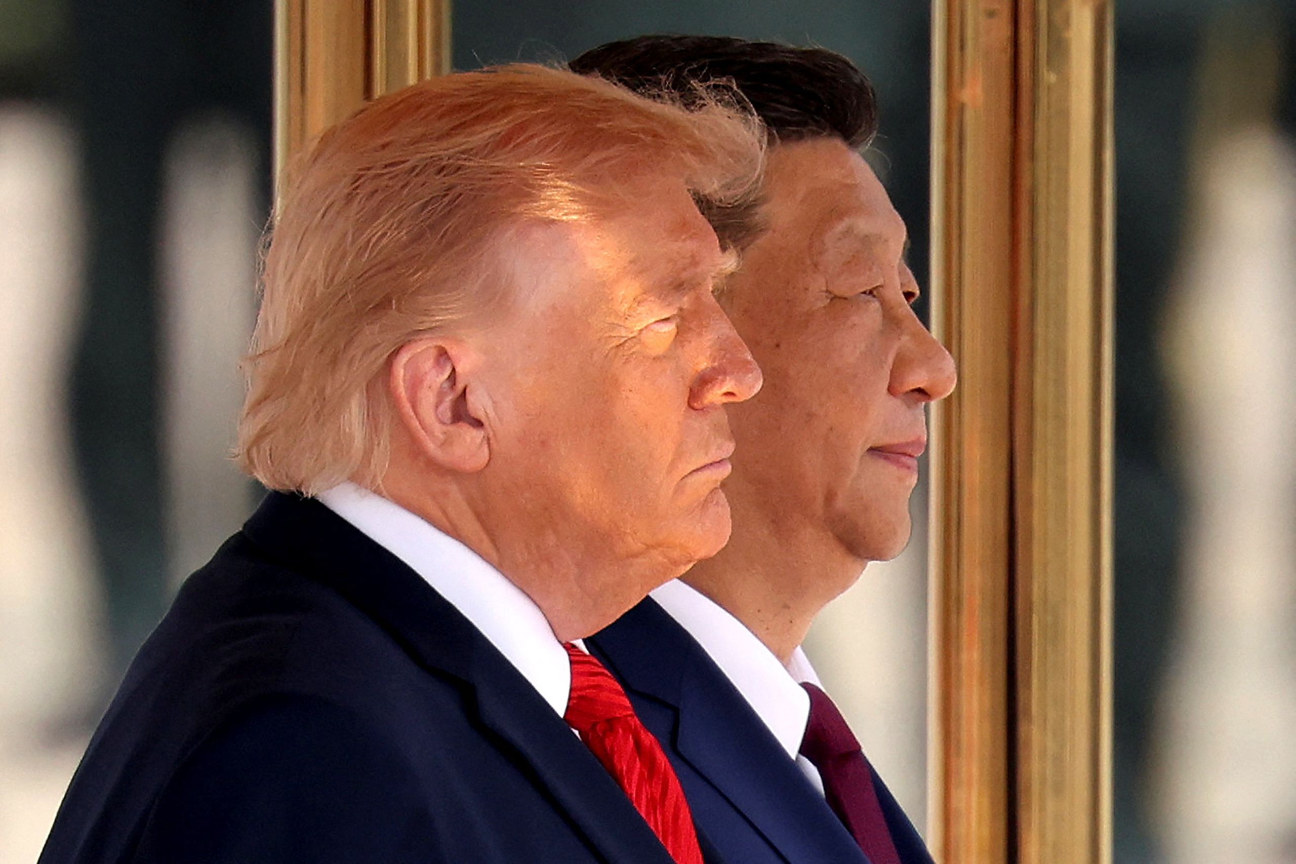 Trump and Xi stand in profile side by side in dark suits before a gold-trimmed doorway.