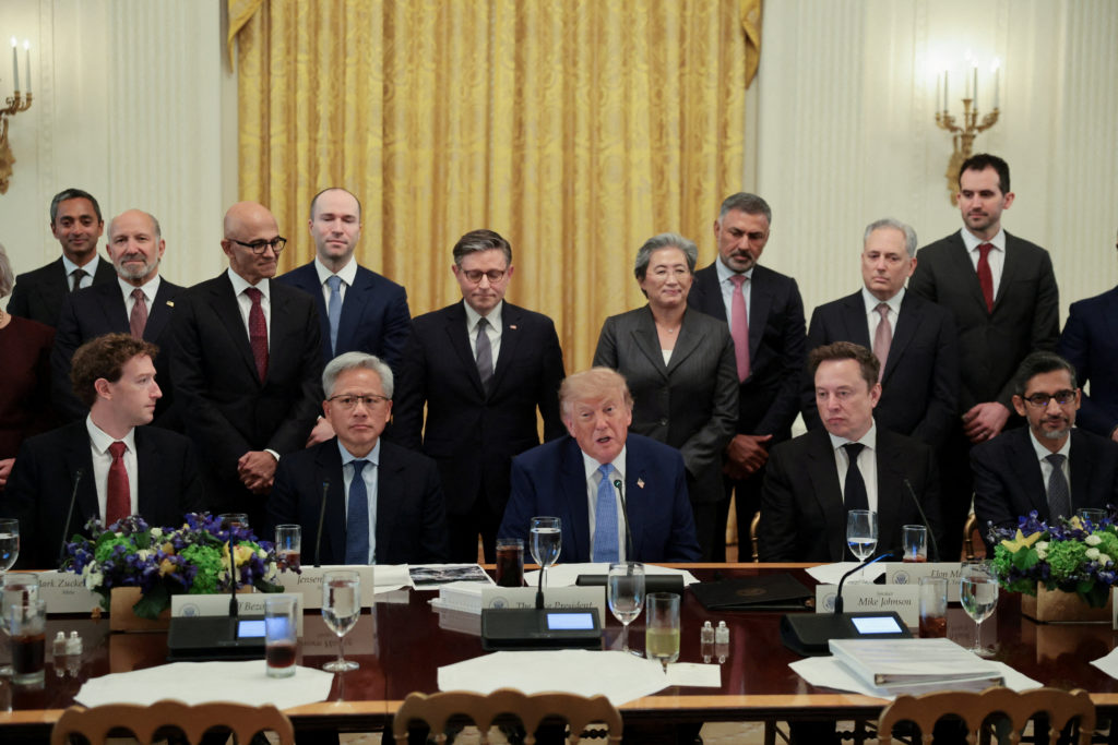 Trump sits at a long table in a gold-curtained White House room, technology executives and officials seated and standing around him.