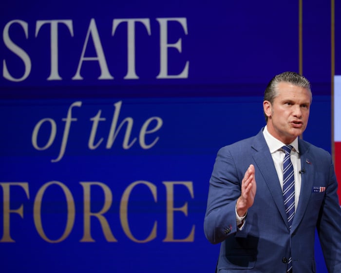 Hegseth gestures while speaking on a stage before a backdrop reading “State of the Force.”