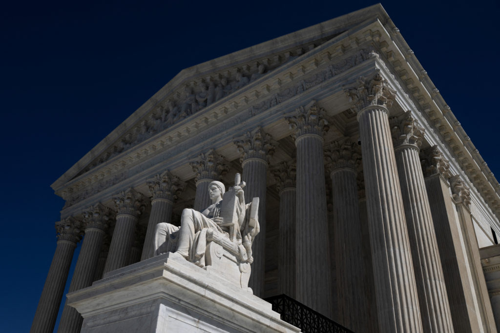 The Supreme Court's columned facade and a seated marble statue, seen from below against a deep blue sky.