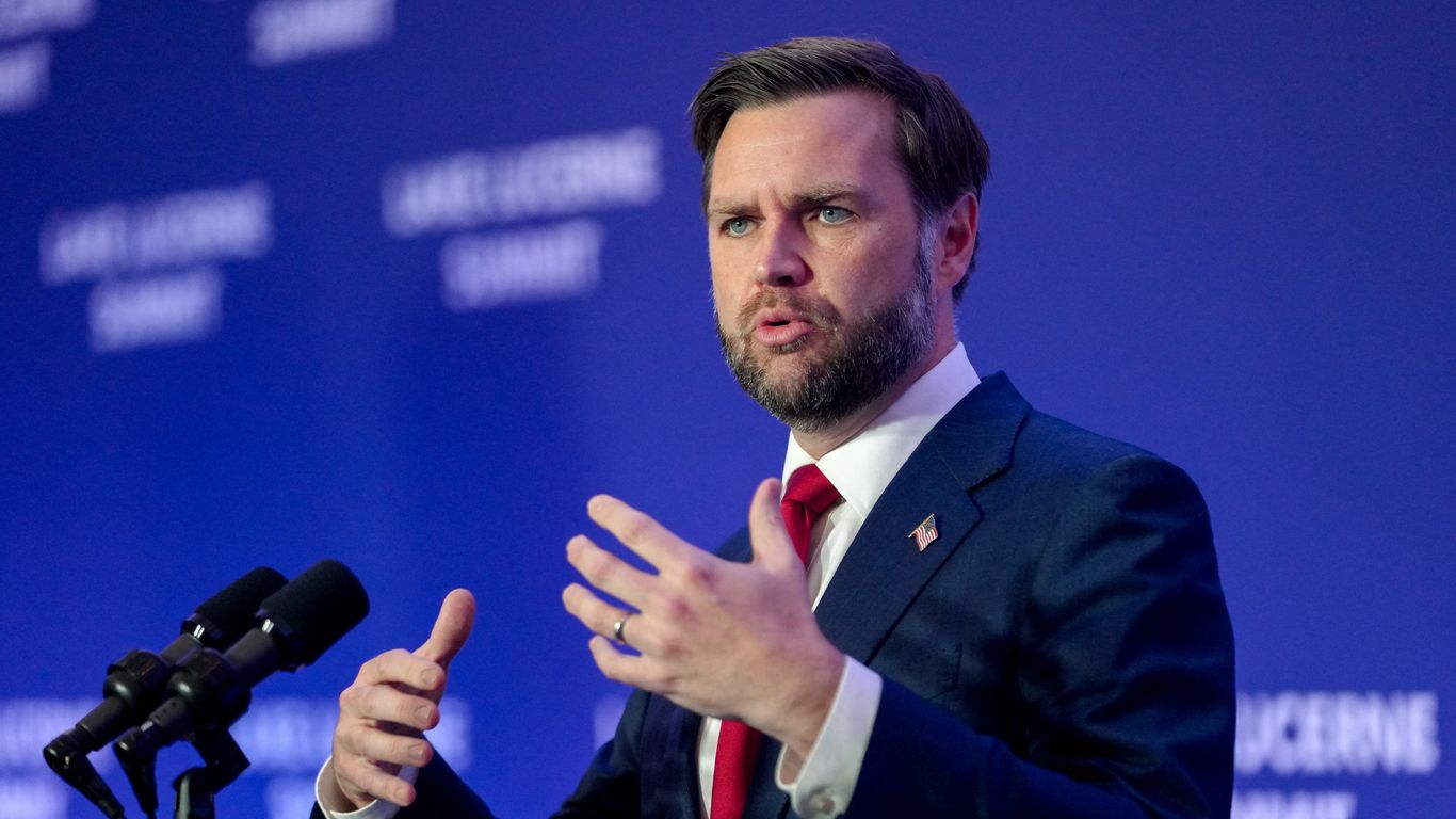 Vice President JD Vance gestures while speaking behind two microphones against a blue backdrop.