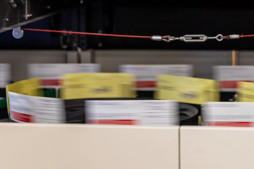 Envelopes printed with red stripes blur past on a sorting machine beneath a taut red cable.