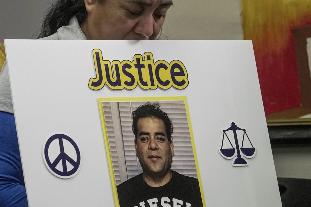 A woman with her head bowed holds a white poster reading “Justice” around a man’s portrait, between a peace sign and a scales-of-justice icon.