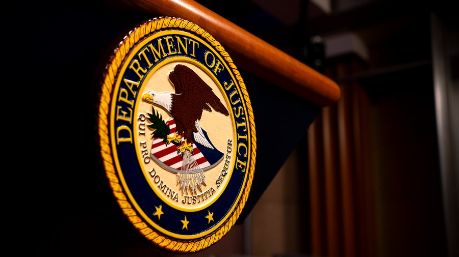 The Department of Justice seal is mounted on the front of a dark lectern beneath a wooden rail.